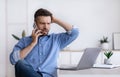 Frustrated businessman having problems with computer, talking on cellphone with customer support Royalty Free Stock Photo