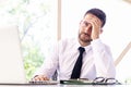 Frustrated businessman sitting at office desk and working on laptop