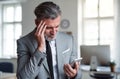 A frustrated businessman with smartphone standing in an office, reading bad news. Royalty Free Stock Photo
