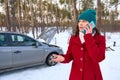 Frustrated Caucasian woman driver talks on mobile phone, calls roadside assistance standing in a snow covered road against her Royalty Free Stock Photo