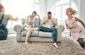 Frustrated couple, children and running in living room chaos with headache in stress on sofa at crazy or busy home