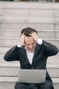 Frustrated and depressed young business man sitting on stairs while working with his laptop Royalty Free Stock Photo