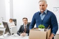Frustrated elderly employee leaving office with box full of belongings