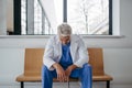 Frustrated, exhausted doctor sitting on bench in hospital corridor. Concept of burnout syndrome among doctors.