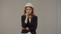 Frustrated female architect, nervous, worried, biting fingers. Redhaired woman in a protective helmet and business suit Royalty Free Stock Photo
