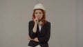 Frustrated female architect, nervous, worried, biting fingers. Redhaired woman in a protective helmet and business suit Royalty Free Stock Photo