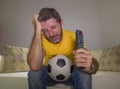 Frustrated football fan in intense emotion - home portrait of young dejected and sad man watching soccer game on television at