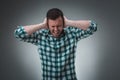 Frustrated handsome man covering his ears with hands standing against gray background.