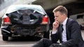 Frustrated man sitting road on crashed car background, traffic accident stress