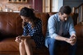 Frustrated married couple sit on couch after quarrel avoid talking