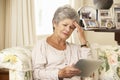 Frustrated Retired Senior Woman Sitting On Sofa At Home Using Digital Tablet Royalty Free Stock Photo