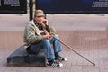 Frustrated Sad Elderly Man with stick sitting on street in solitude and looking at camera.