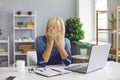 Upset senior woman sitting at desk with laptop and covering face unable to deal with problem