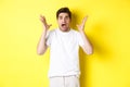 Frustrated and shocked guy panicking, screaming and looking scared, standing in white t-shirt over yellow background