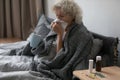 Frustrated sick elderly lady covered with warm blanket