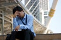 Frustrated stressed Asian businessman with hand on forehead sitting on staircase in the city. Depressed unemployment business conc
