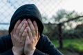 Frustrated teenage boy covering hes face in front of correctional institutes wired fence