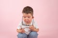 Frustrated toddler removes glasses from face,close up portrait on pink. Child failure concept.