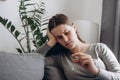 Frustrated unhappy desperate woman sits on sofa holding engagement ring in hand, stressed young female suffering from relations