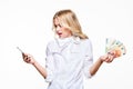 Frustrated woman looking in disbelief at her mobile phone, holding loads of Euro banknotes against white background. Phone bill. Royalty Free Stock Photo