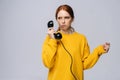 Frustrated woman in stylish yellow sweater holding handset receiver of retro phone and looking away Royalty Free Stock Photo