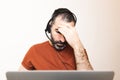 Frustrated young beard man with his hand on his forehead keeping eyes closed at his working place in home