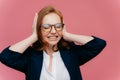 Frustrated young businesswoman has headache, ignores loud noise, covers ears with hands, clenches teeth, has closed eyes, wears Royalty Free Stock Photo