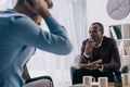 Frustrated young man sititng on sofa and african american psychiatrist