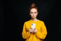 Frustrated young woman holding mobile phone and looking at camera on isolated black background. Royalty Free Stock Photo