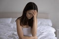 Frustrated young woman sitting on bed suffering from sudden headache