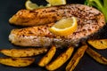 Fryed salmon fillets background on a black plate with lemon slice, french fries and boiled broccoli. Grilled salmon