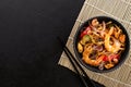 Frying asian wok noodles with prawns and mussels in a black bowl and chopsticks on a black slate background Royalty Free Stock Photo