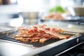 frying bacon strips on a flat top stovetop in a commercial kitchen