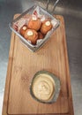 Frying basket full of fried balls and a small bowl of sauce served on wooden tray