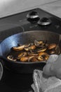 Frying chestnut mushrooms, with a man holding a cast iron frying pan with a tea towel, on an electric hob Royalty Free Stock Photo