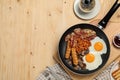 Frying pan with cooked traditional English breakfast and cup of coffee on wooden table, flat lay. Space for text Royalty Free Stock Photo