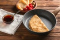 Frying pan with delicious thin pancakes and syrup on wooden table