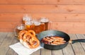 Frying pan with roasted sausages, beer mugs and glasses and soft salted pretzels on aged wooden table. Selective focus Royalty Free Stock Photo