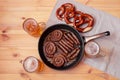 Frying pan with roasted sausages, beer mugs and soft salted pretzels on wooden table Royalty Free Stock Photo