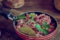 A frying pan with stewed meat seasoned with fresh herbs on a wooden countertop. Royalty Free Stock Photo