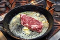 Frying pan on a stove on which a large piece of meat is fried with butter