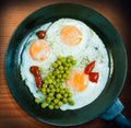 A frying pan with three fried eggs as well as peas and ketchup on a wooden background Royalty Free Stock Photo