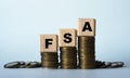 FSA - acronym on wooden cubes. Which stand on stacks of coins on a light background