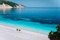 Fteri beach, Kefalonia, Greece. Lonely unrecognizable tourist couple hiding from sun umbrella chill relax near clear