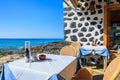 MORRO JABLE, FUERTEVENTURA - FEB 7, 2014: tables and chairs of a restaurant on coast of Morro Jable town. Building is made of lava Royalty Free Stock Photo