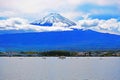 Fujiyama mountain before the lake with trees, houses, buildings, bridge, and ships .