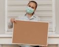 A young woman in a mask shows a finger on a blank cork board, standing on a white background. Copy space on whiteboard for image o Royalty Free Stock Photo