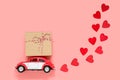 Fulda, Germany - DEC 18, 2020: Small red retro toy car delivering gift box for Valentine`s day on pink background with hearts