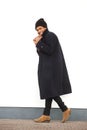 Full body african american male fashion model walking and smiling with winter jacket and beaning by white wall Royalty Free Stock Photo