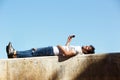 Full body cheerful man lying on wall with headphones and cellphone Royalty Free Stock Photo